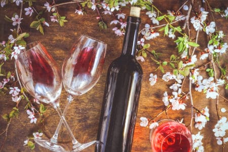 A bottle of wine, glasses with red wine and the flowering branch of fruit tree