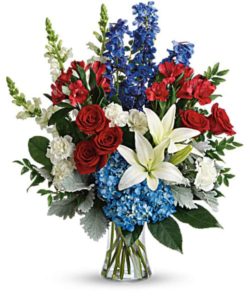This bouquet features blue hydrangea, red roses, white asiatic lilies, red alstroemeria, white carnations, blue delphinium, white snapdragons, huckleberry, dusty miller, aralia leaf and lemon leaf. Delivered in a gathering vase.