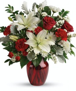 This beloved bouquet includes red roses, white asiatic lilies, red carnations, red miniature carnations, white cushion spray roses, white sinuata statice, dusty miller, huckleberry, and lemon leaf. Delivered in a ruby rose vase. Approximately 16 1/2" W x 18" H